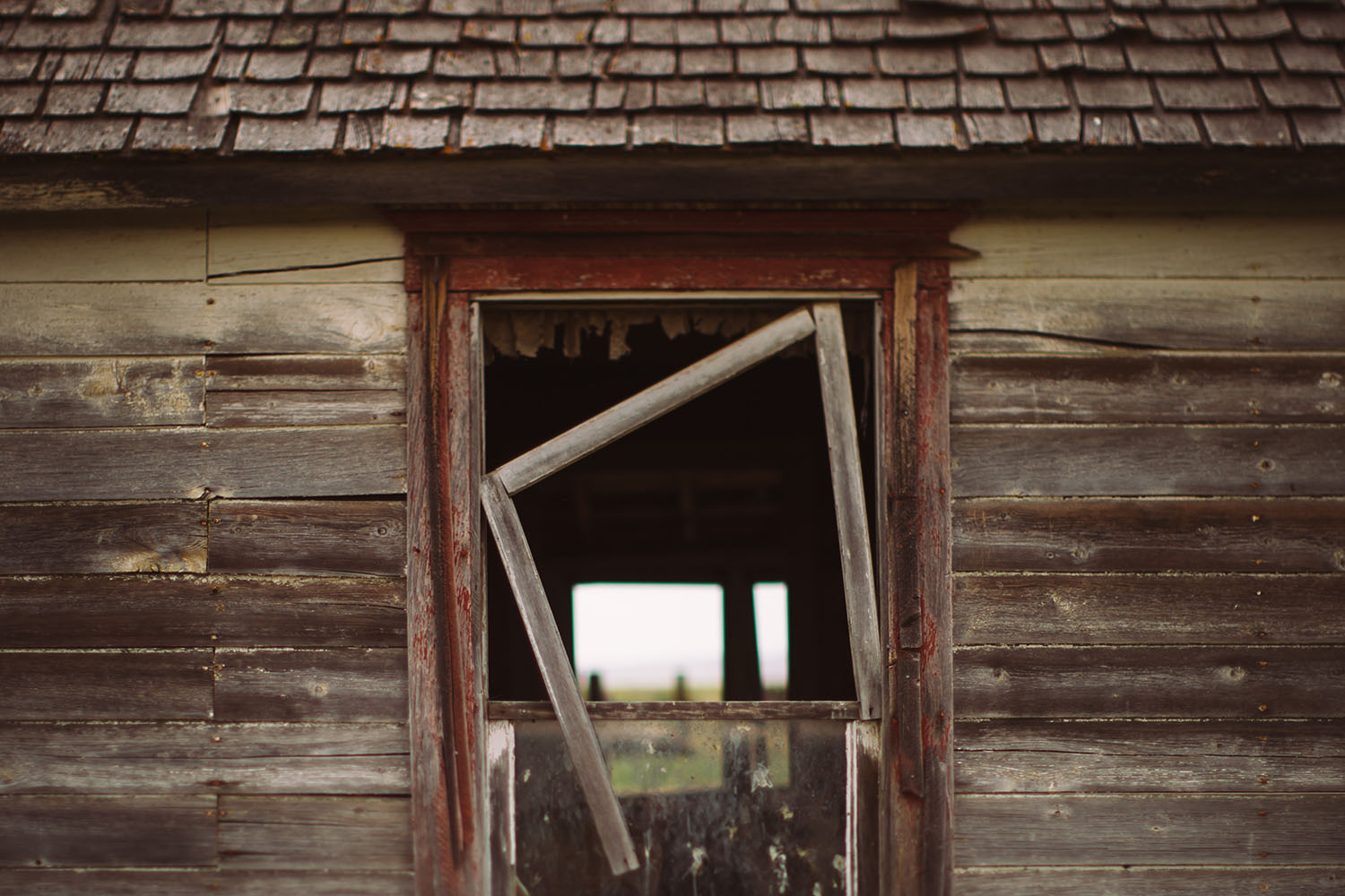 The bent frame of an old window rests crookedly in its hole in an abandoned Montana outbuilding